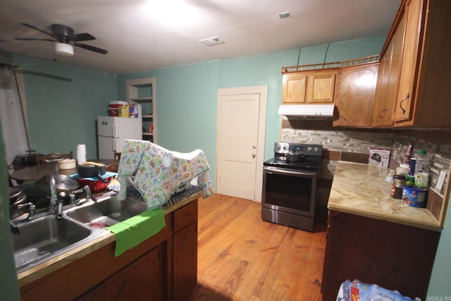 kitchen with stainless steel range with electric cooktop, freestanding refrigerator, light wood-style flooring, a ceiling fan, and backsplash