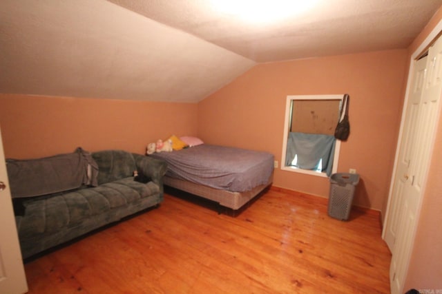 bedroom with light wood finished floors, lofted ceiling, and a closet