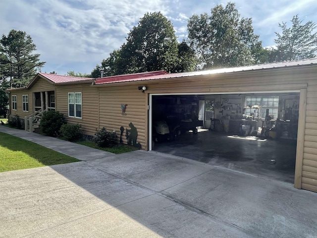 view of front of property featuring driveway, an attached garage, faux log siding, and metal roof