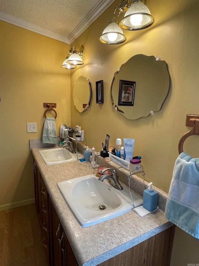 bathroom featuring a textured ceiling, ornamental molding, hardwood / wood-style floors, and double vanity