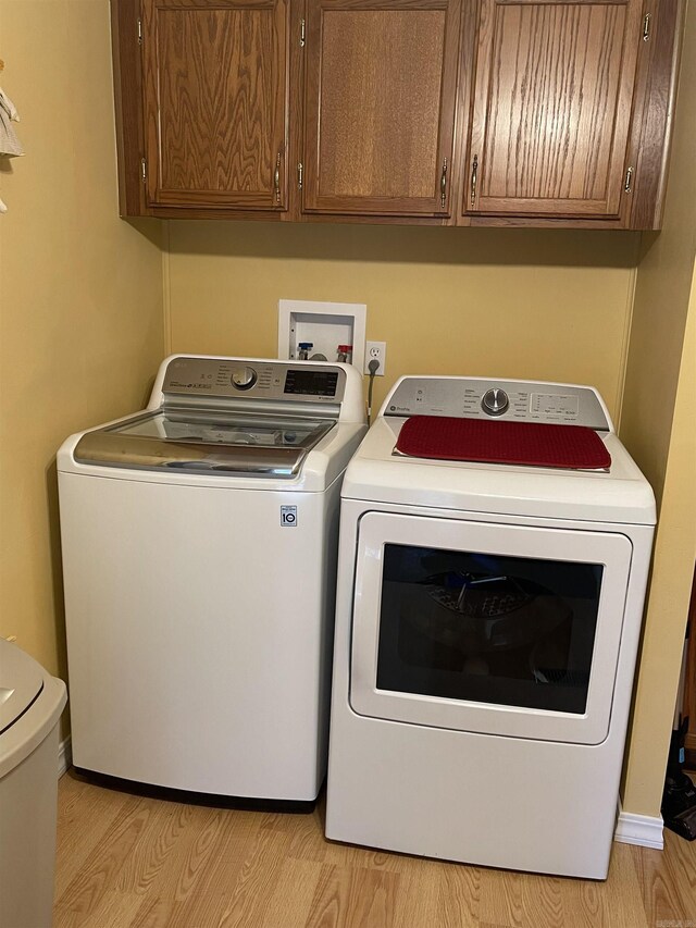 laundry room featuring light hardwood / wood-style floors, washing machine and dryer, hookup for a washing machine, and cabinets