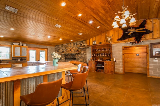 interior space with stainless steel dishwasher, tile countertops, wood walls, a fireplace, and wood ceiling