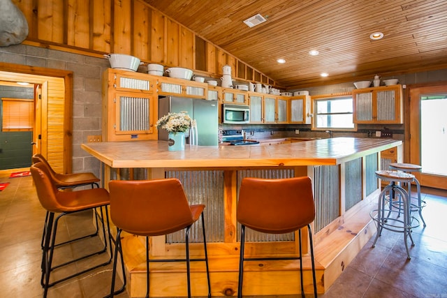 kitchen featuring appliances with stainless steel finishes, a kitchen breakfast bar, wooden ceiling, lofted ceiling, and wood walls