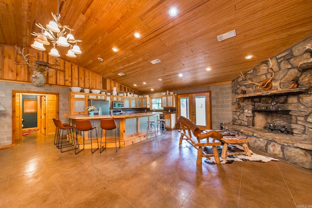 kitchen with appliances with stainless steel finishes, vaulted ceiling, wooden ceiling, a stone fireplace, and wood walls