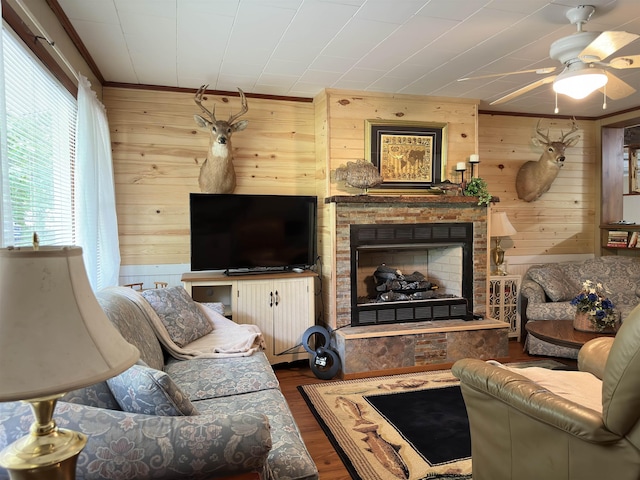 living room with ceiling fan, a stone fireplace, dark hardwood / wood-style flooring, wood walls, and ornamental molding