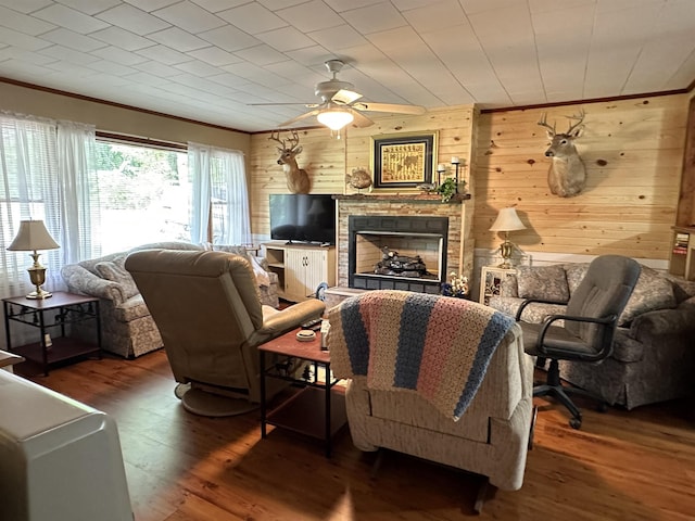 living room with a stone fireplace, wooden walls, dark hardwood / wood-style floors, ceiling fan, and ornamental molding