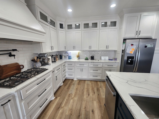 kitchen with decorative backsplash, appliances with stainless steel finishes, premium range hood, and white cabinetry