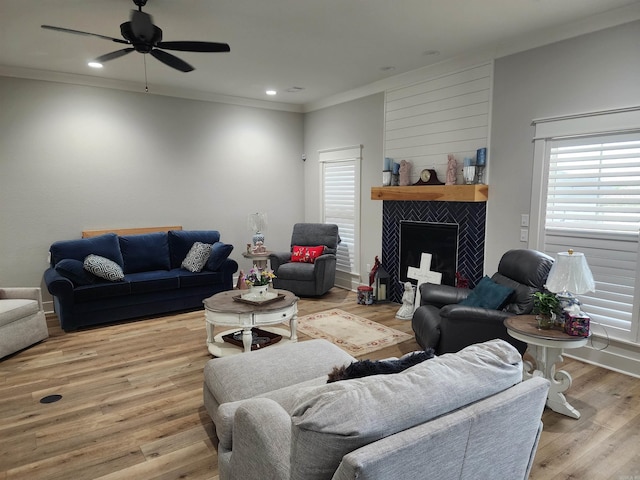 living room featuring a tiled fireplace, ceiling fan, light hardwood / wood-style floors, and ornamental molding