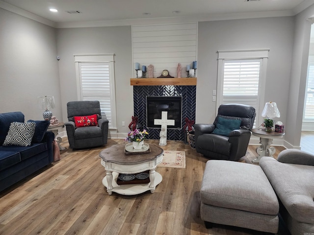 living room with light hardwood / wood-style floors, ornamental molding, and a tiled fireplace