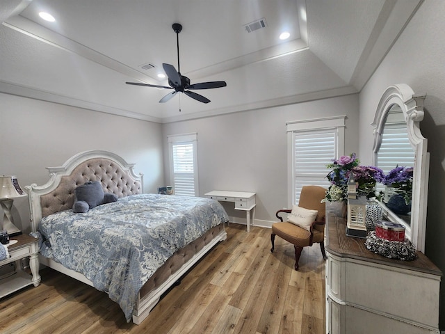 bedroom with hardwood / wood-style floors, ceiling fan, a raised ceiling, and crown molding