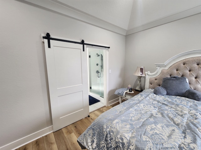 bedroom featuring a barn door, vaulted ceiling, and light wood-type flooring