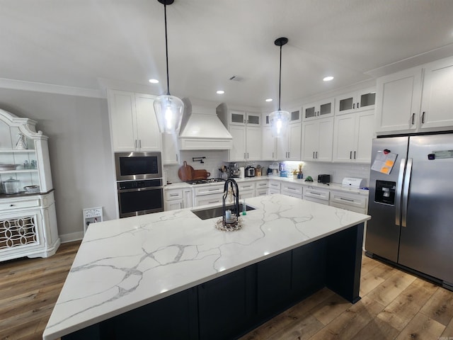 kitchen with sink, an island with sink, stainless steel appliances, and custom range hood