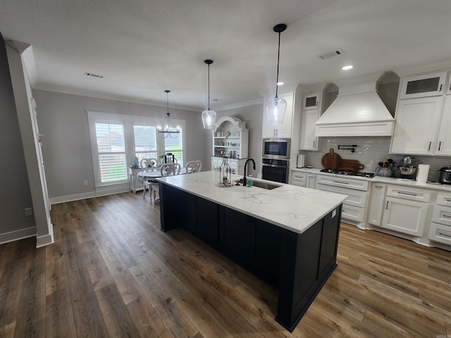 kitchen with white cabinets, appliances with stainless steel finishes, an island with sink, and custom exhaust hood