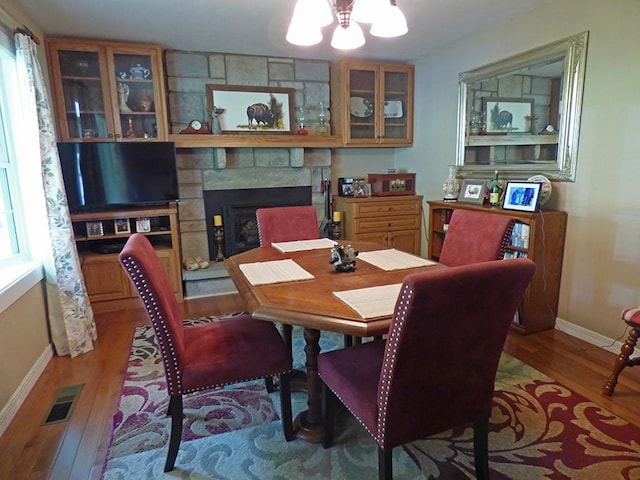 dining room with a stone fireplace, a healthy amount of sunlight, and hardwood / wood-style floors