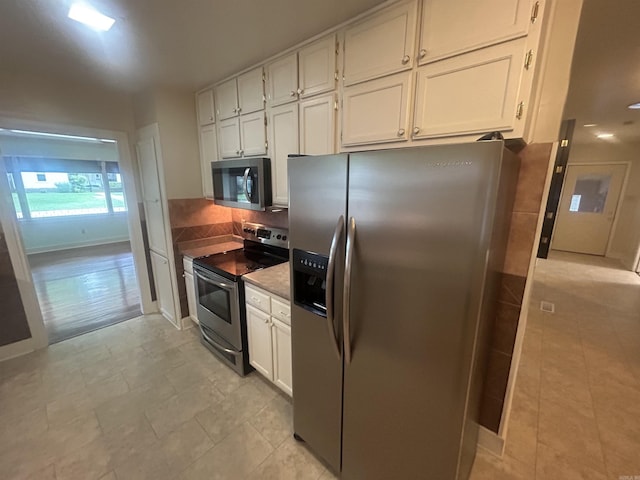 kitchen with backsplash, appliances with stainless steel finishes, white cabinetry, and baseboards