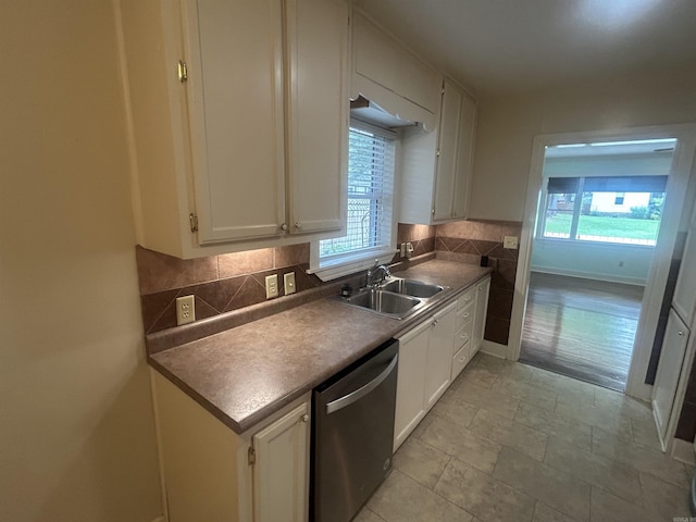 kitchen featuring a sink, tasteful backsplash, stainless steel dishwasher, white cabinetry, and baseboards