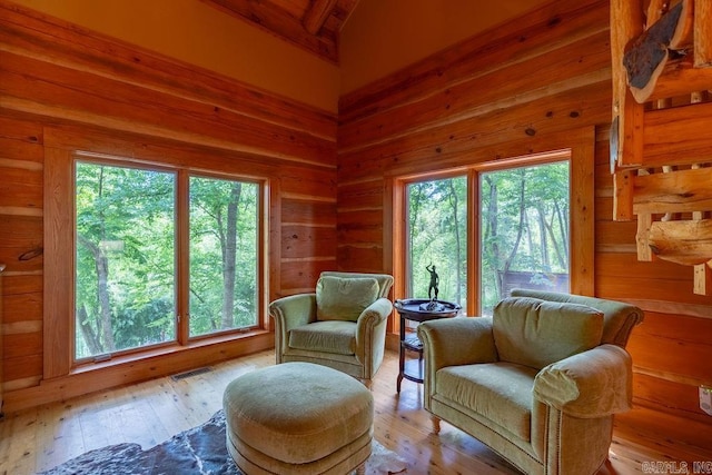 living area featuring vaulted ceiling with beams, wood walls, and light hardwood / wood-style flooring