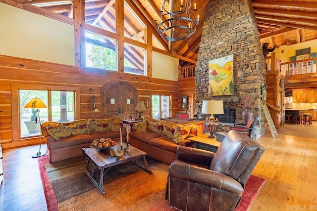 living room with wood walls, high vaulted ceiling, a stone fireplace, a notable chandelier, and wood-type flooring