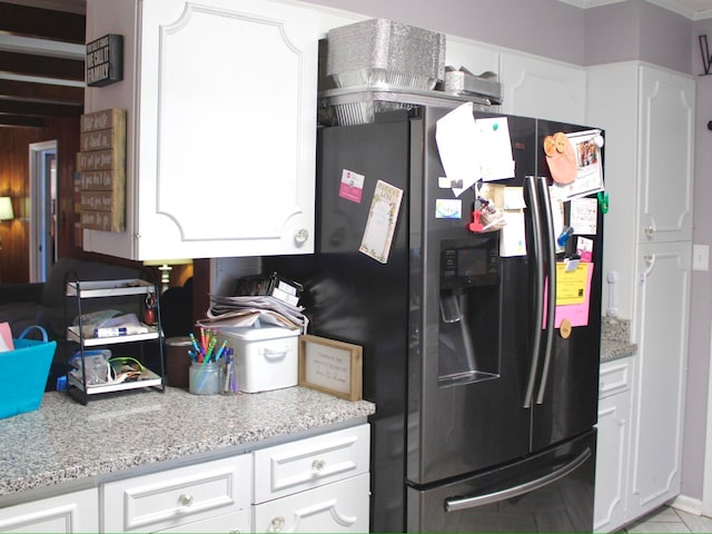 kitchen featuring black fridge with ice dispenser, light tile flooring, light stone countertops, ornamental molding, and white cabinets