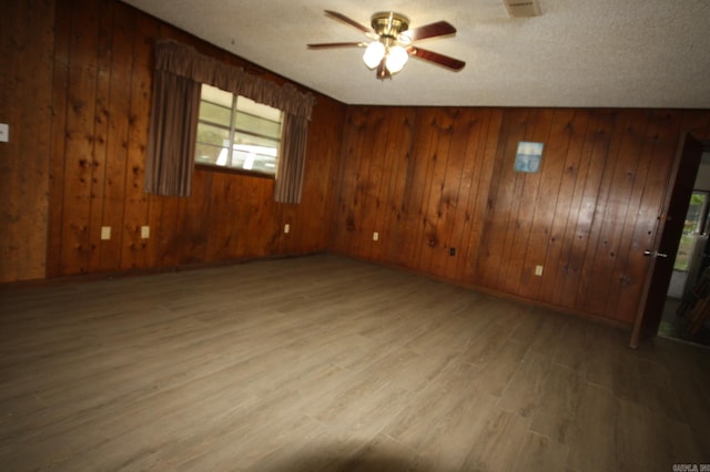 empty room with ceiling fan, vaulted ceiling, wood-type flooring, a textured ceiling, and wooden walls