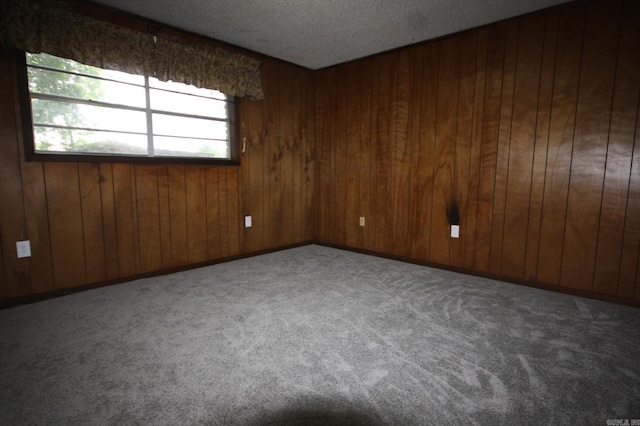 empty room with carpet, a textured ceiling, and wood walls