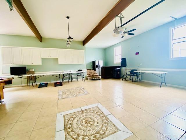 interior space featuring baseboards, beamed ceiling, ceiling fan, and light tile patterned floors