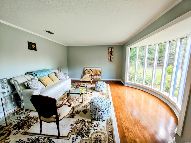 living room with wood finished floors, a textured ceiling, baseboards, visible vents, and ornamental molding