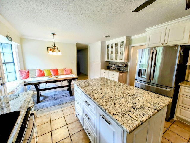 kitchen with stainless steel fridge with ice dispenser, a kitchen island, light stone counters, visible vents, and glass insert cabinets