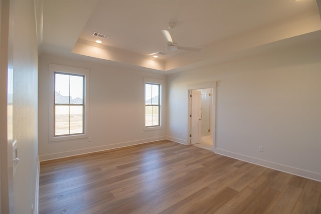 empty room featuring ceiling fan, a tray ceiling, and light hardwood / wood-style floors