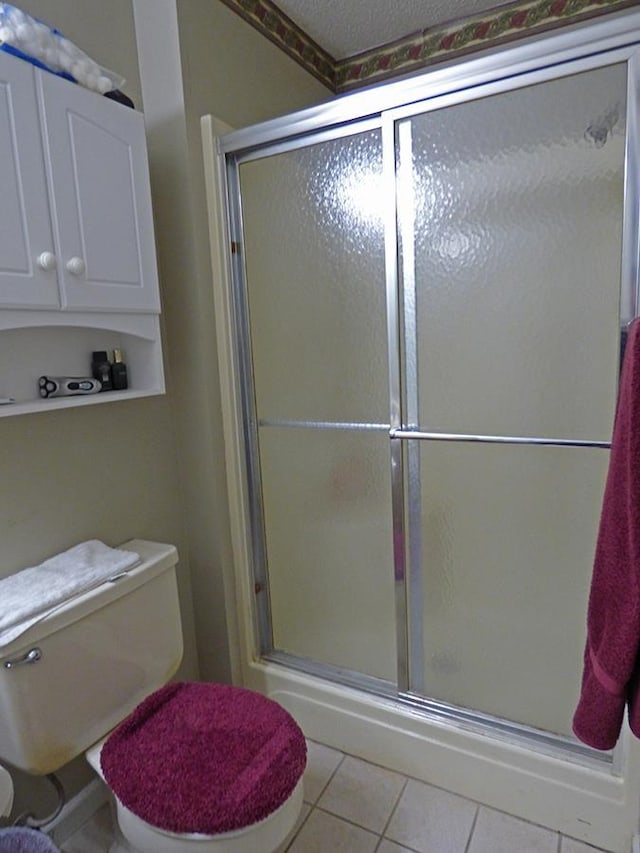 bathroom with tile patterned flooring, toilet, and a shower with door