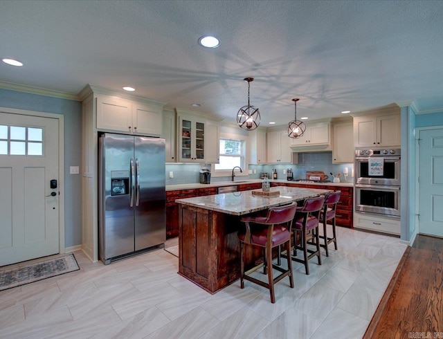 kitchen with sink, light stone counters, decorative light fixtures, a kitchen island, and appliances with stainless steel finishes