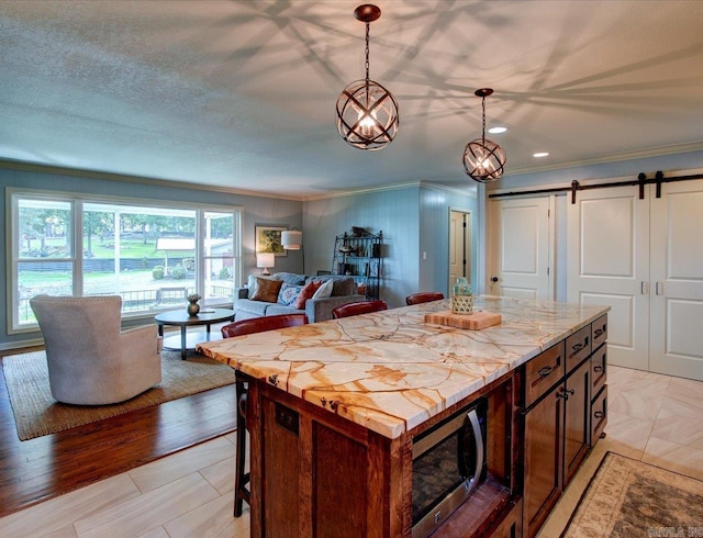 kitchen featuring crown molding, a barn door, light stone countertops, decorative light fixtures, and a kitchen island