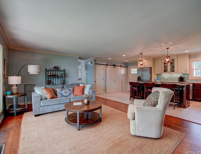 living room featuring a barn door, light hardwood / wood-style floors, crown molding, and a notable chandelier