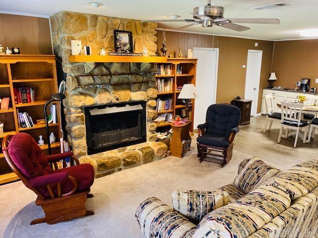 carpeted living room featuring ceiling fan, crown molding, and a fireplace