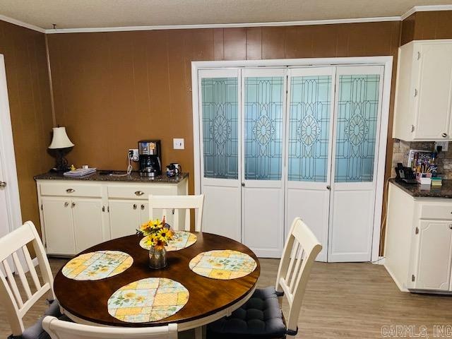 dining area with ornamental molding, light hardwood / wood-style floors, and wood walls