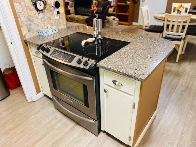 kitchen featuring light stone countertops, backsplash, electric range, white cabinetry, and light hardwood / wood-style flooring