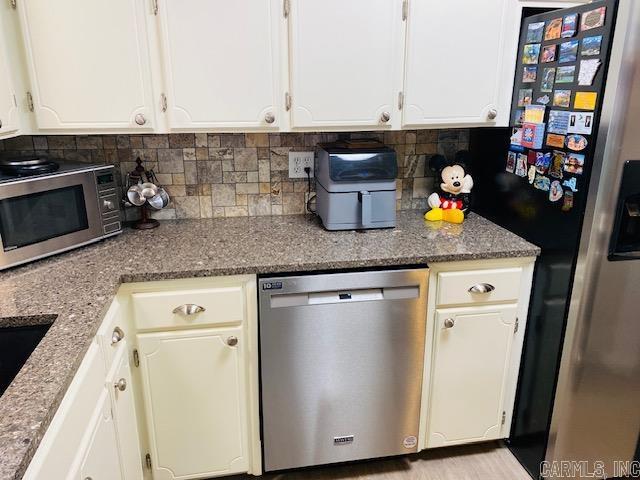 kitchen featuring appliances with stainless steel finishes, white cabinetry, stone counters, and backsplash