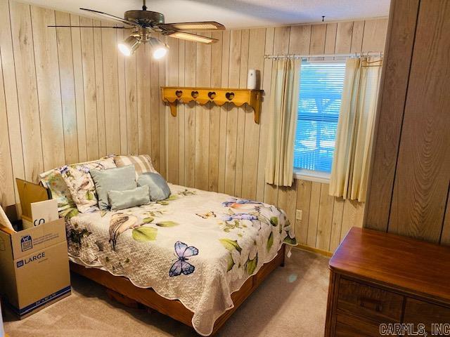 carpeted bedroom with ceiling fan and wood walls