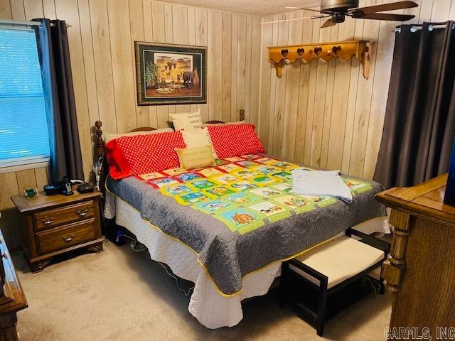 carpeted bedroom featuring wood walls and ceiling fan