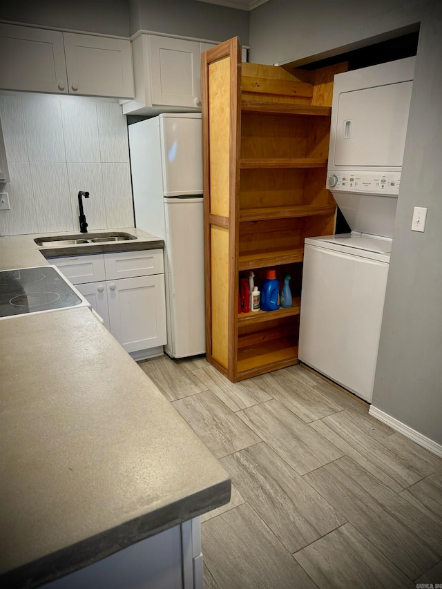 kitchen with white cabinetry, stacked washer / drying machine, backsplash, sink, and white fridge