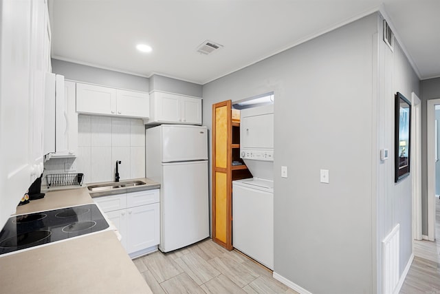 kitchen with white cabinets, stacked washer and dryer, backsplash, sink, and white fridge