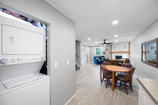 clothes washing area featuring ceiling fan, stacked washer / drying machine, light wood-type flooring, a brick fireplace, and brick wall