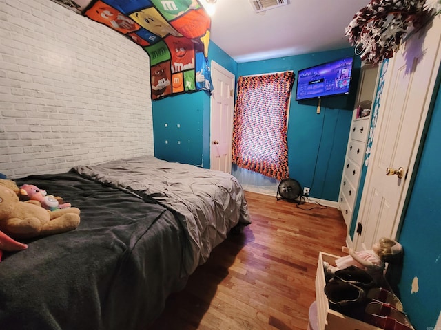 bedroom featuring wood-type flooring and brick wall