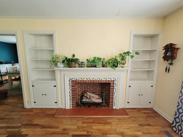 living room featuring built in shelves, ornamental molding, wood-type flooring, and a tile fireplace