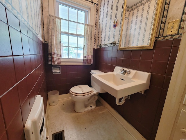 bathroom with heating unit, sink, tile walls, and toilet