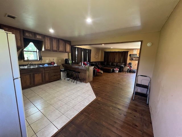 kitchen featuring dark brown cabinetry, light hardwood / wood-style floors, sink, and white refrigerator