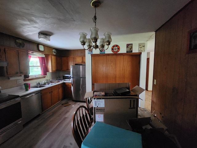 kitchen with pendant lighting, hardwood / wood-style floors, sink, appliances with stainless steel finishes, and a chandelier