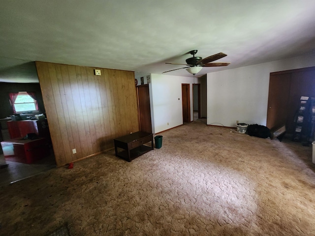 unfurnished living room with carpet flooring, wood walls, and ceiling fan