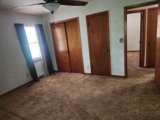 unfurnished bedroom with dark colored carpet, ceiling fan, and two closets