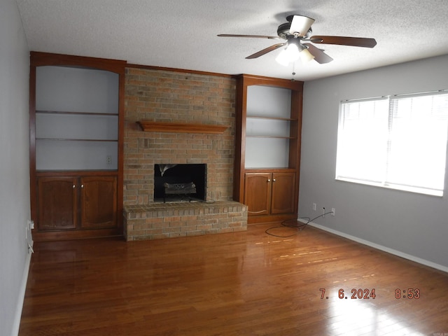 unfurnished living room with ceiling fan, a brick fireplace, built in features, wood-type flooring, and a textured ceiling